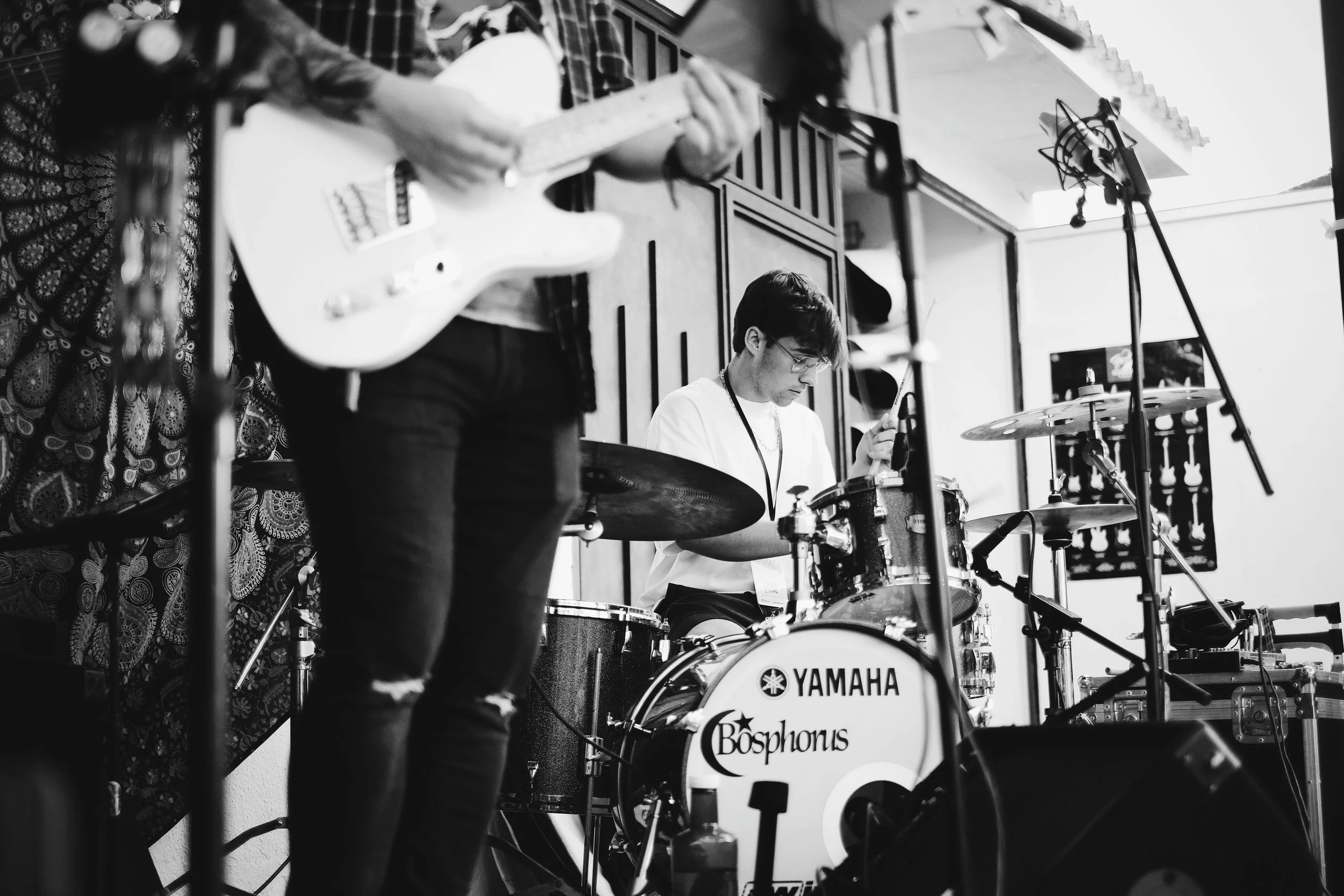 Medio en estudio de grabación, con una persona tocando la batería Yamaha Bosphorus y otra tocando la guitarra.