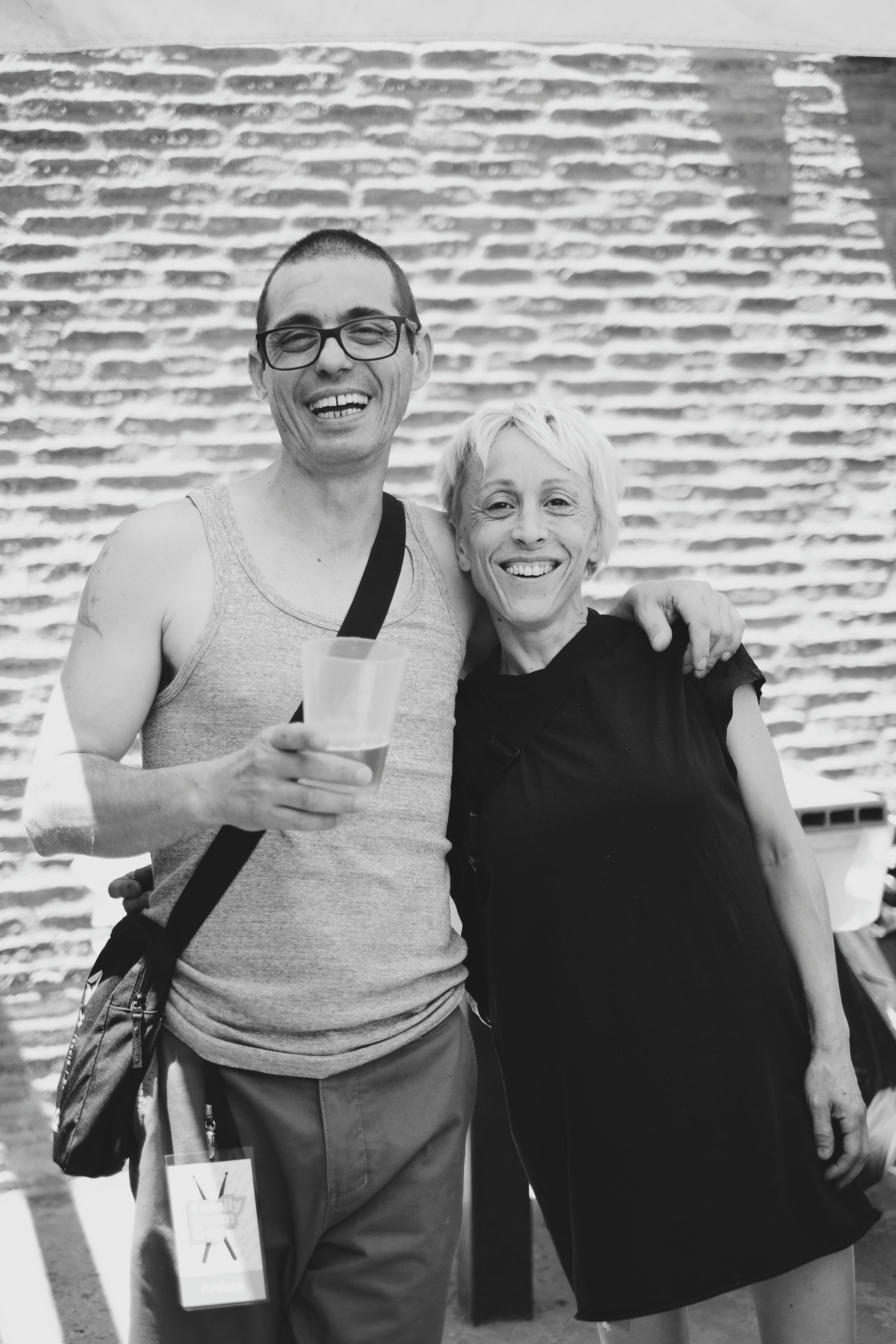 Dos personas sonriendo y abrazadas, una mujer mayor y un joven con gafas, en un entorno urbano, en una foto en blanco y negro.