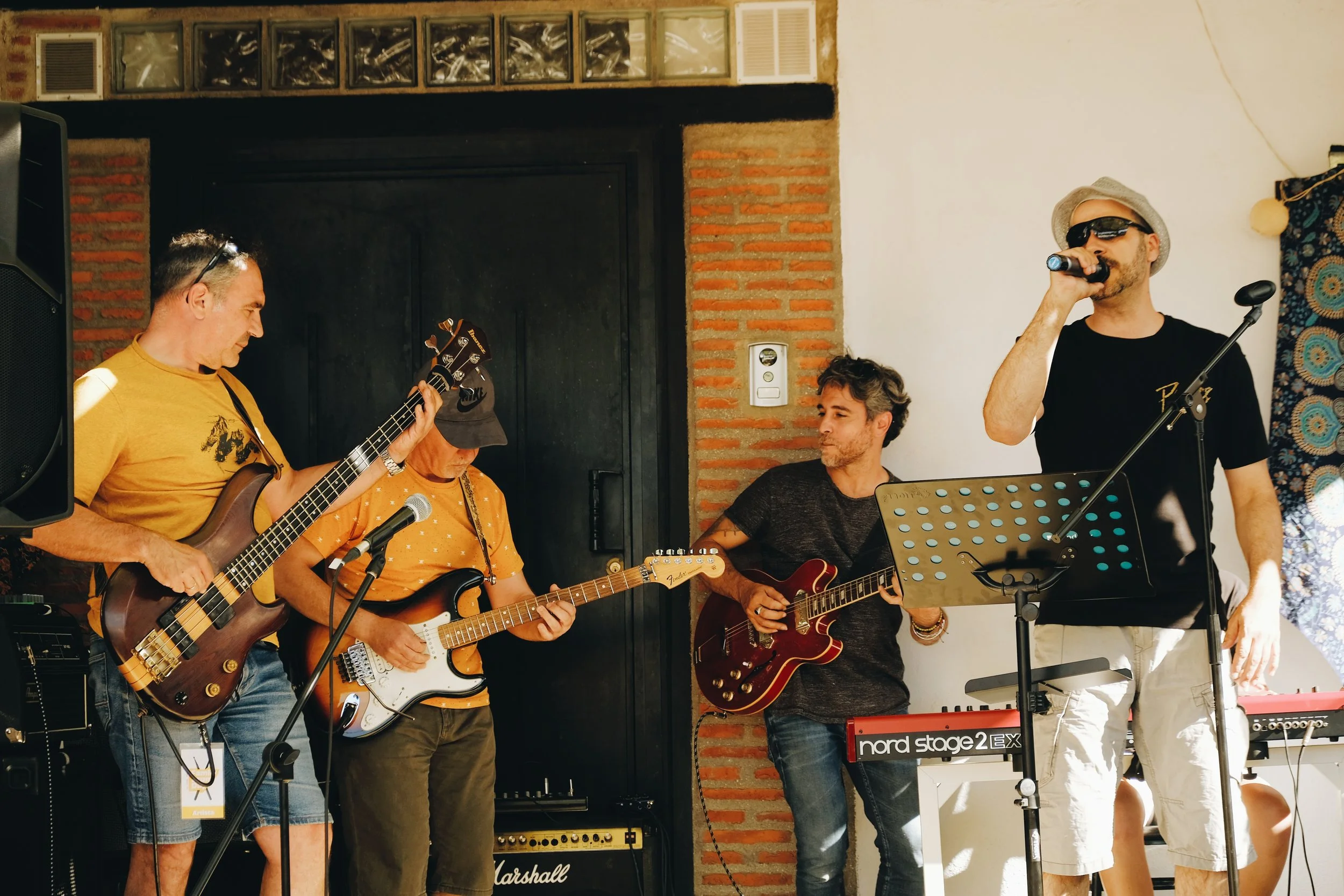 Grupo de músicos tocando en un escenario, con guitarras y micrófono, en un ambiente de interior.
