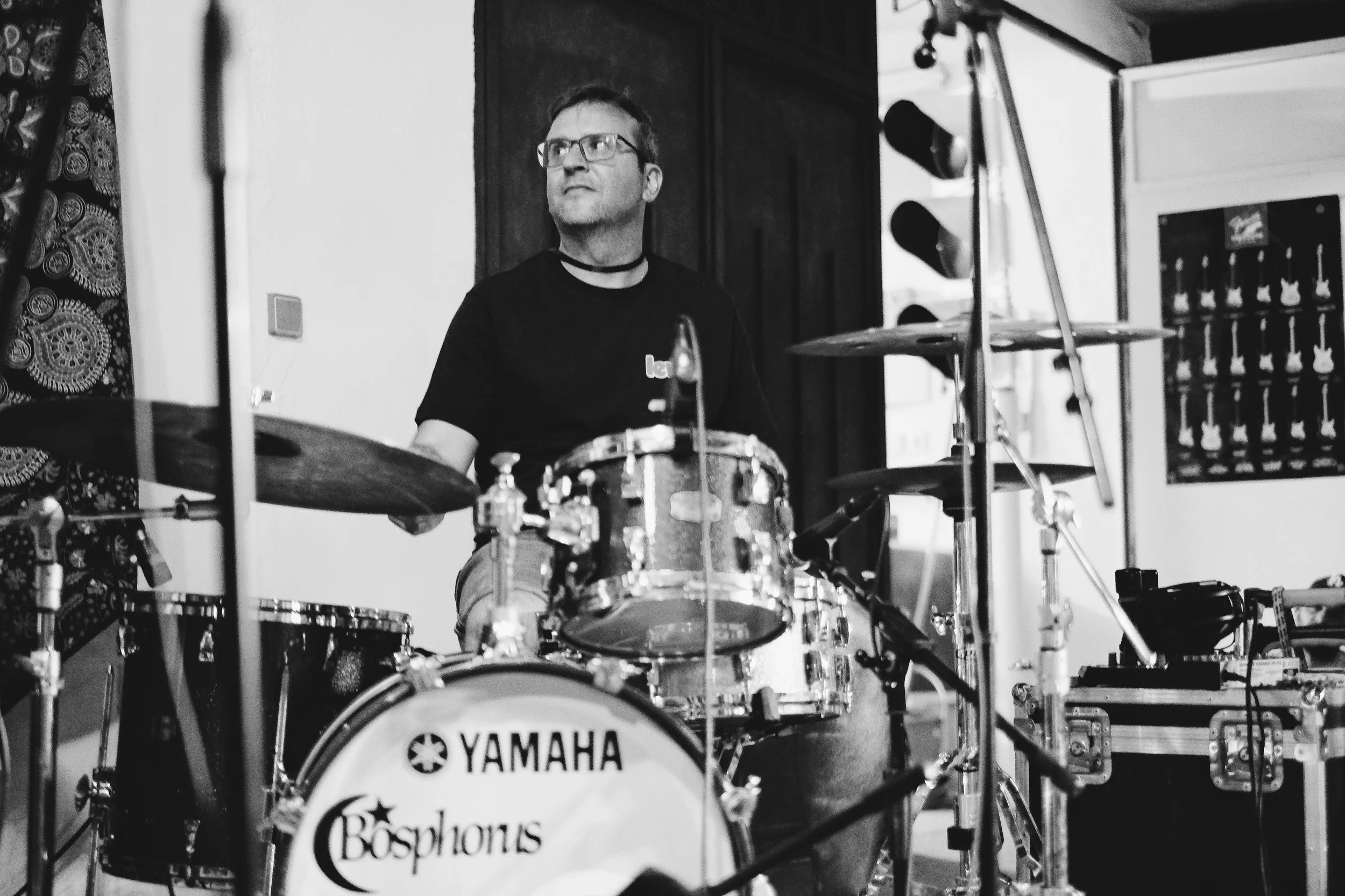 Persona tocando la batería en un estudio de música, en negro y blanco.