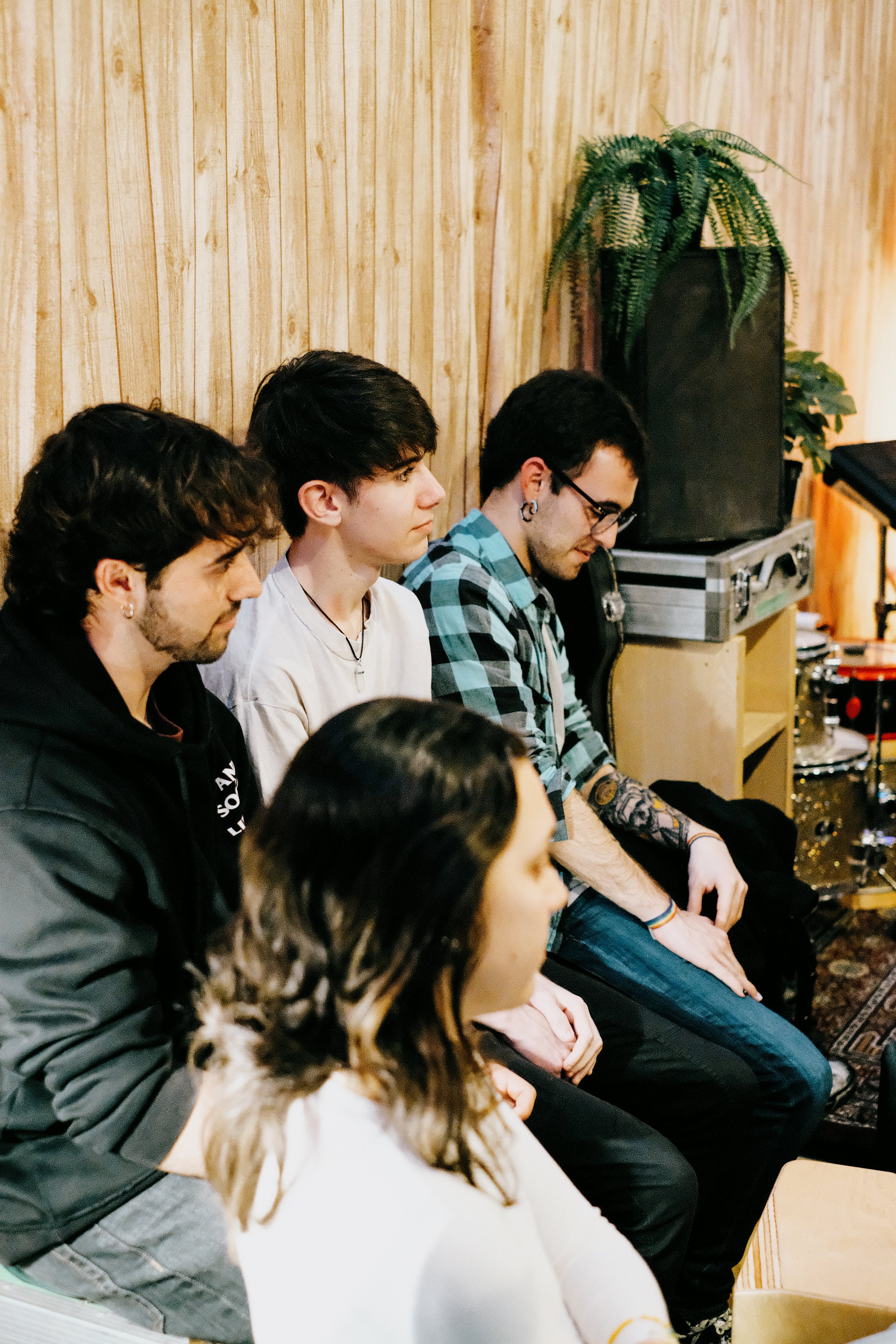 Cinco personas sentadas en un ambiente de grabación, con pared de madera y plantas decorativas en el fondo.