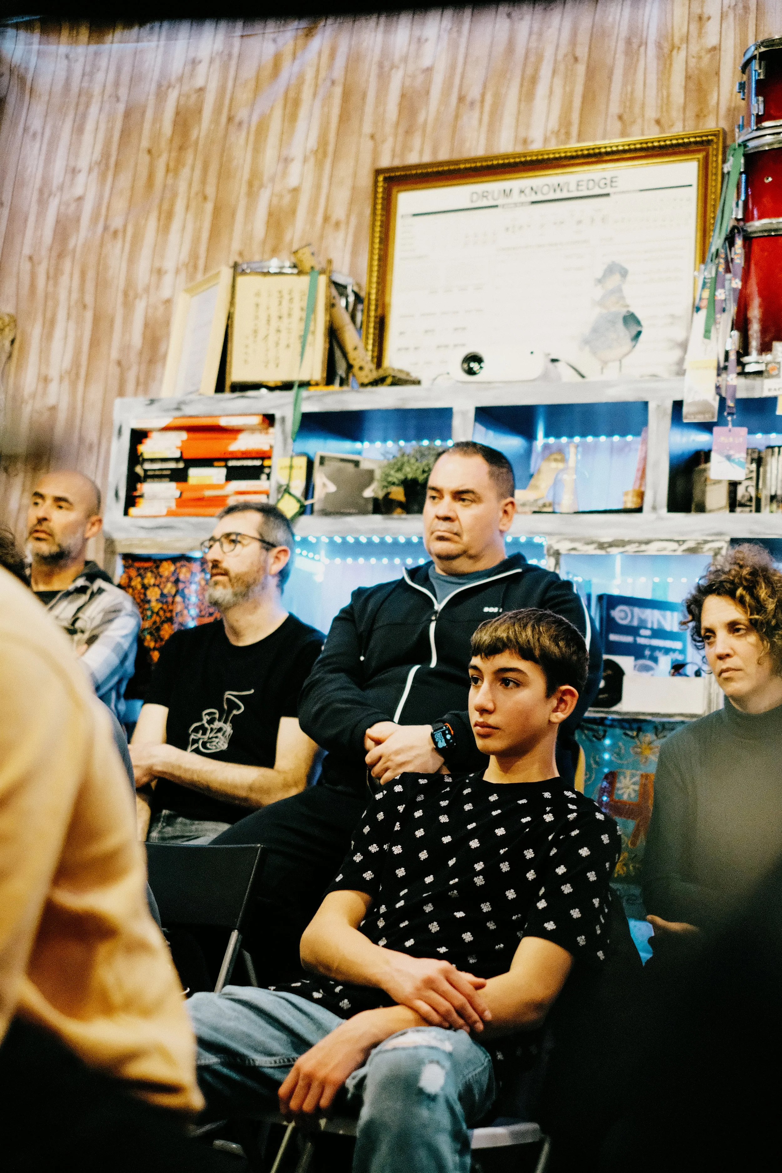 Personas sentadas en una reunión o taller, en un lugar con paredes de madera y decoraciones variadas, algunas con luces de neón.