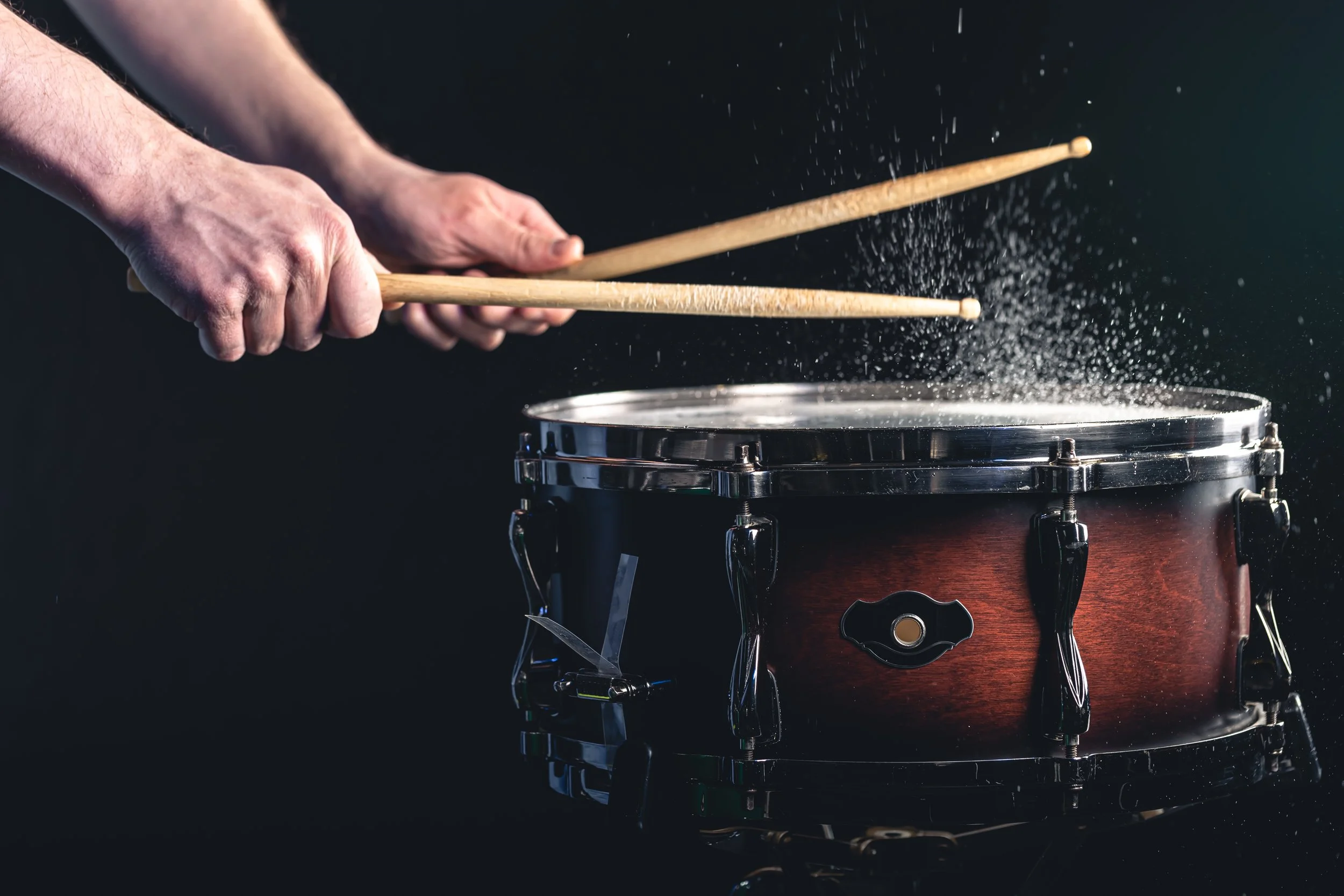 Manos tocando una batería en un escenario oscuro.