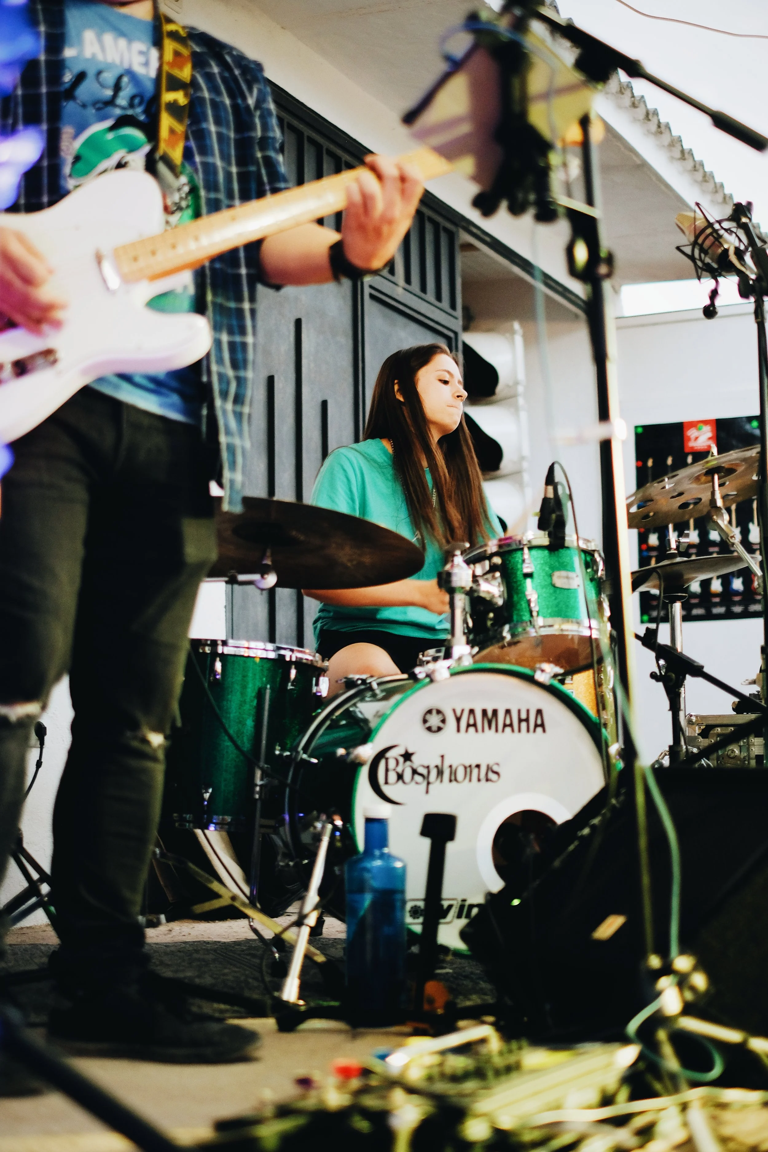 Músicos tocando en un escenario, con un baterista y un guitarrista visible, en un entorno interior.