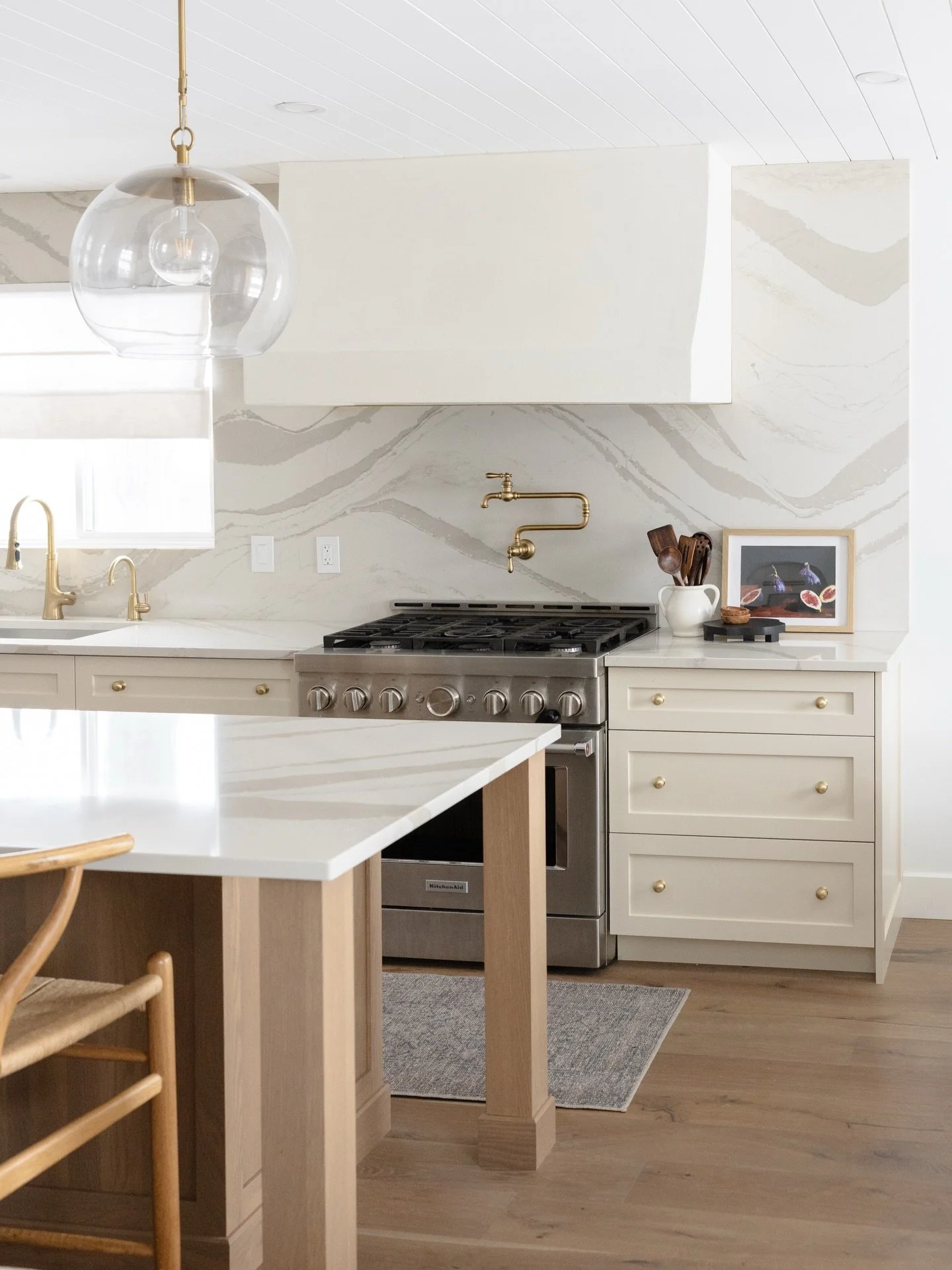 The beauty is in the balance! 

We paired creamy cabinetry with a dramatic stone splash to give Project Little &amp; Light a sense of history and permanence. 

From the silhouette of the custom hood to the living finish on the brass, this kitchen was