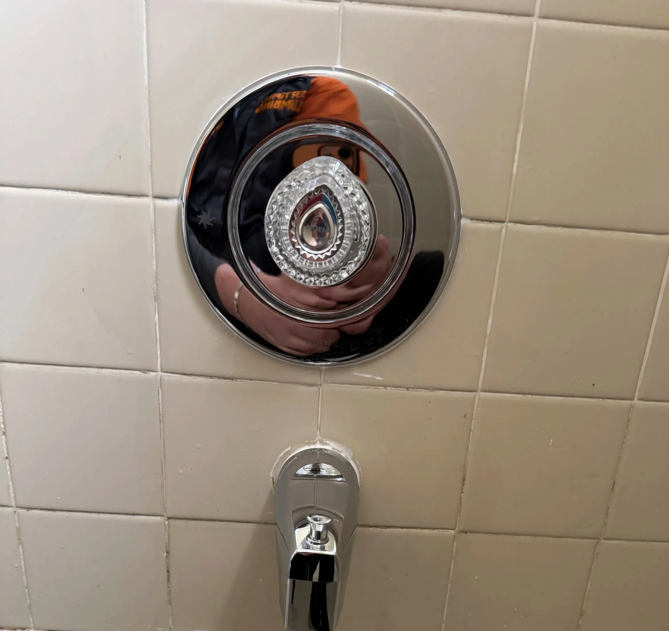 Close-up of a shower control valve and temperature dial mounted on a tiled wall.