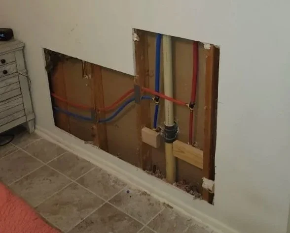 Wall with an open section revealing plumbing pipes and water supply lines.