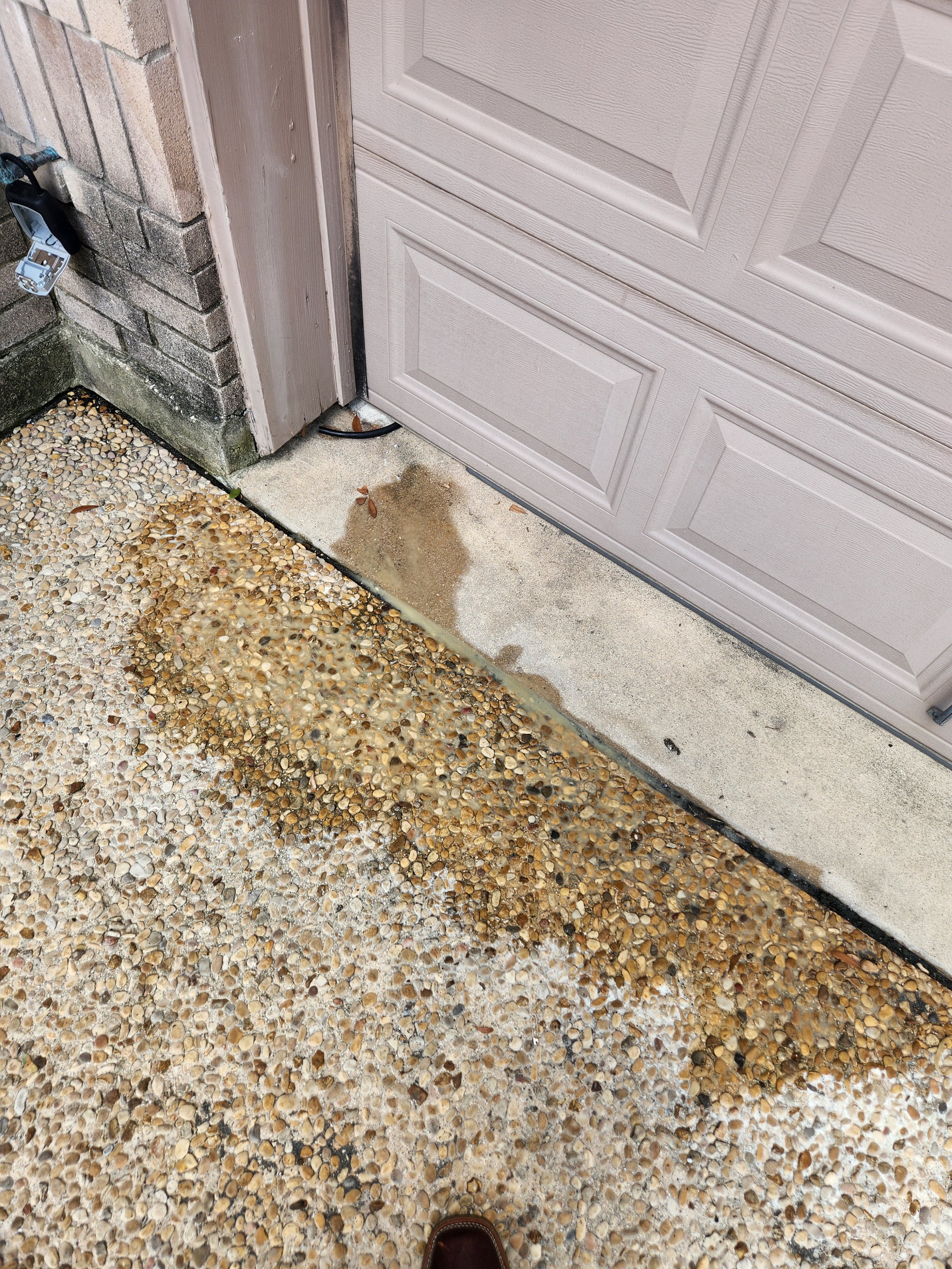 Close-up of a garage door with water stains and a pebble concrete driveway.
