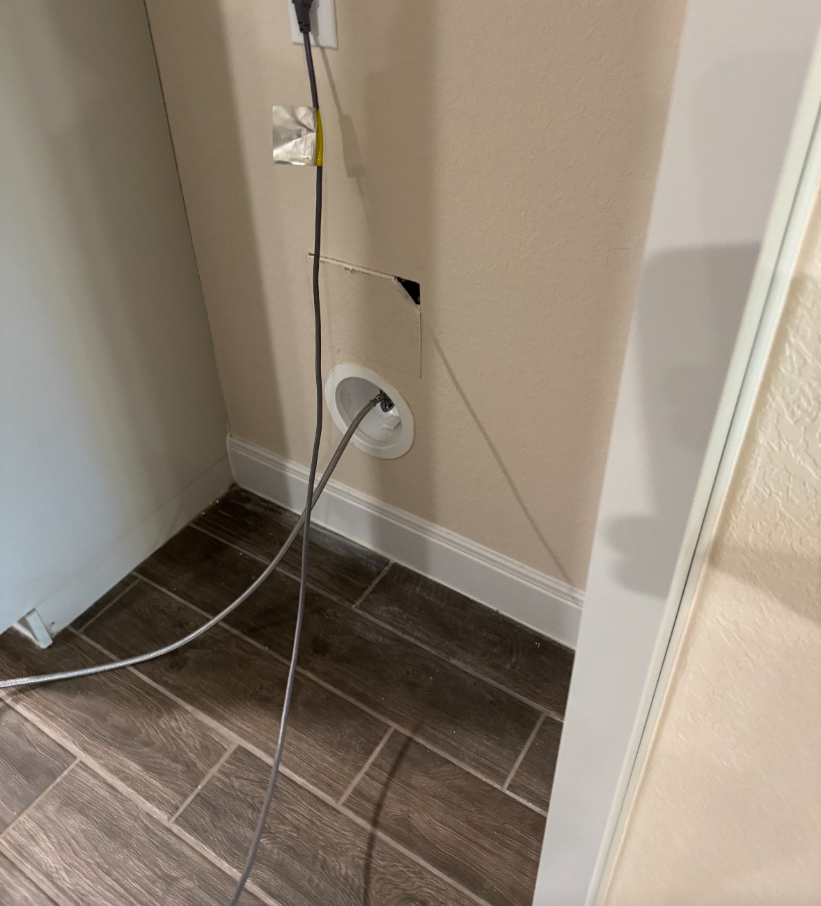 Space behind a refrigerator exposing the power cord and the water line connection.