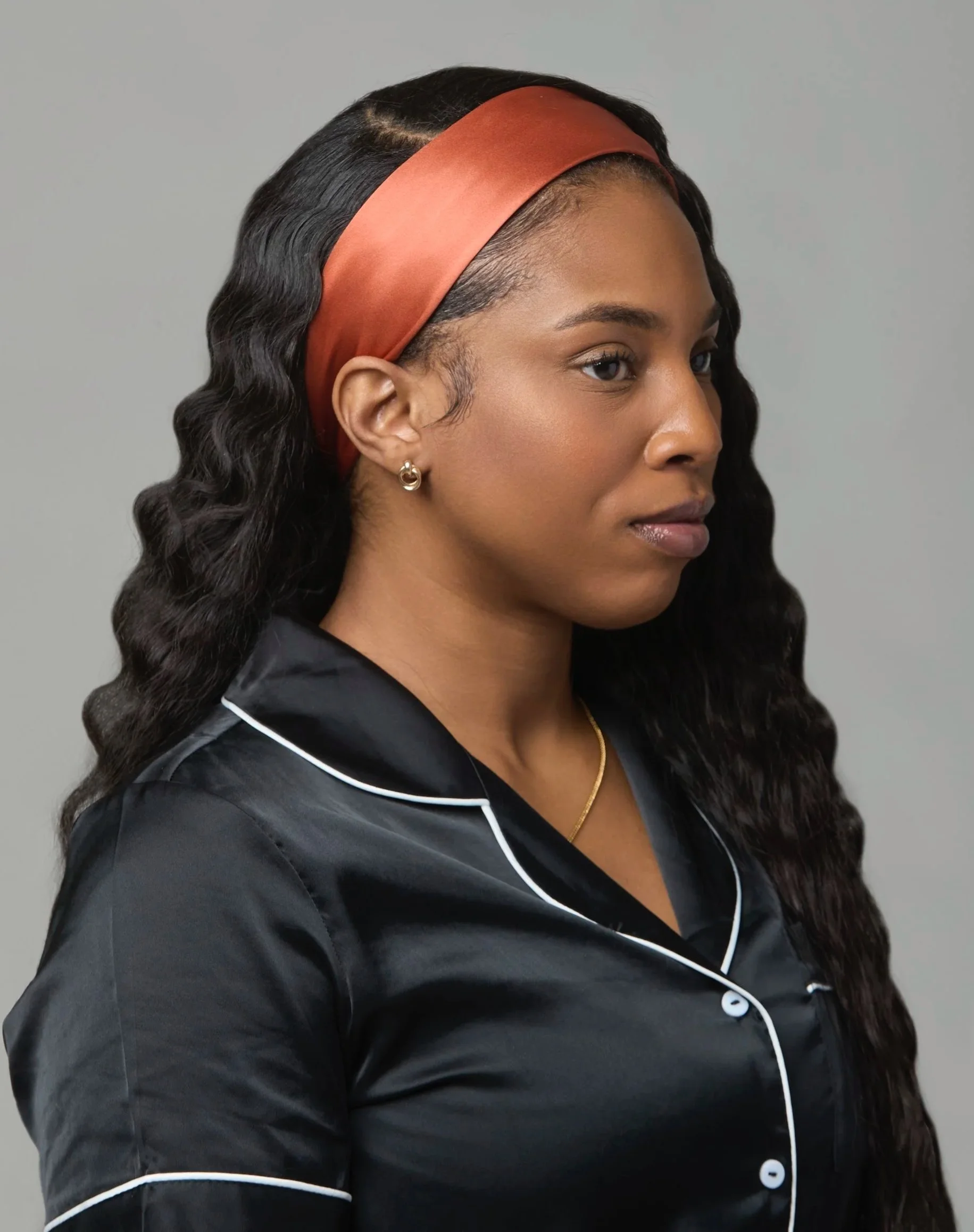 A woman  with long wavy hair wearing a rust/burnt orange silk head band from Select silk, a luxury hair accessory for everyday wear.