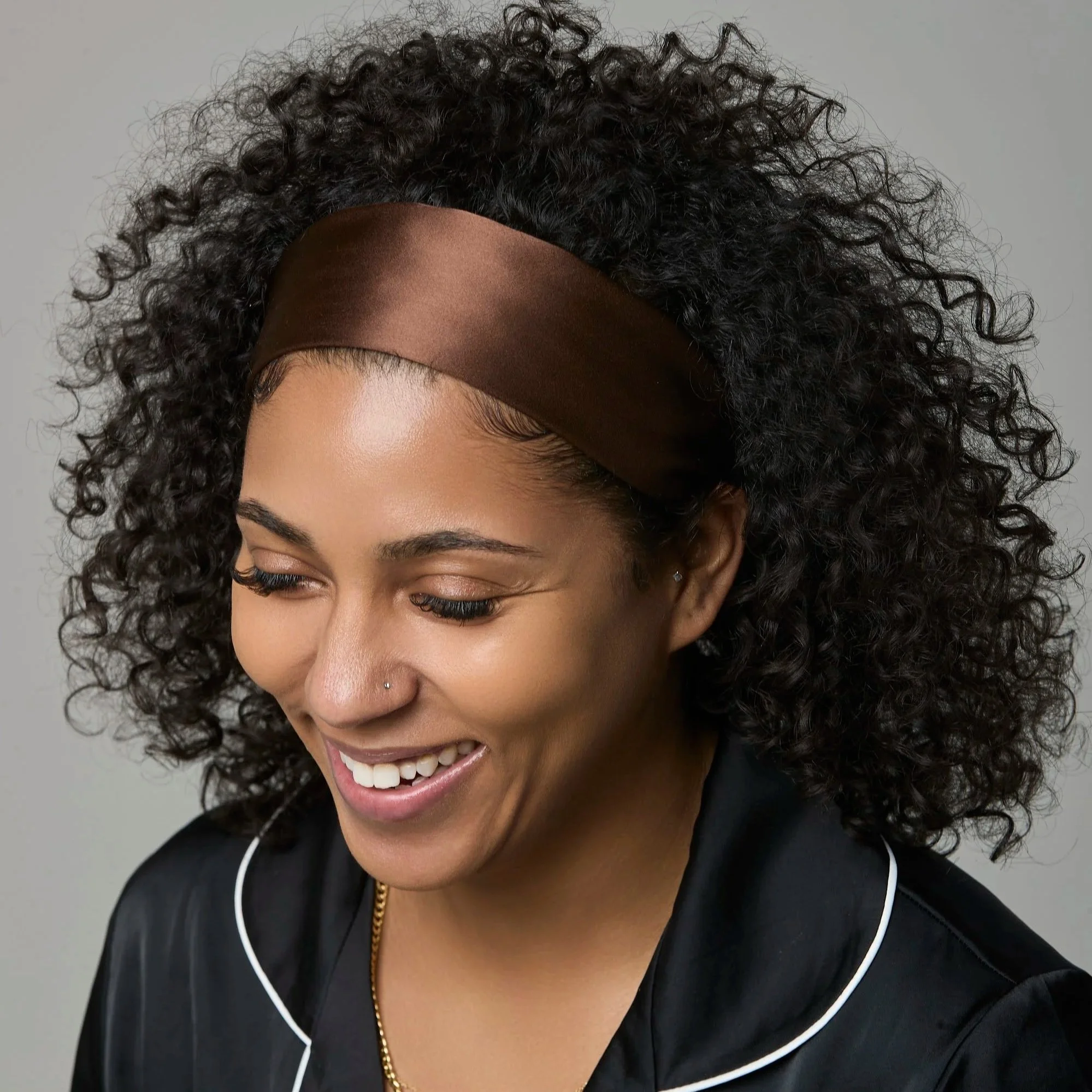 A woman with dark curly hair is wearing a rust/burnt orange silk head band from Select silk, a luxury hair accessory for everyday wear.