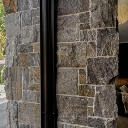 Close-up of a stone wall with a vertical black metal strip dividing the stones