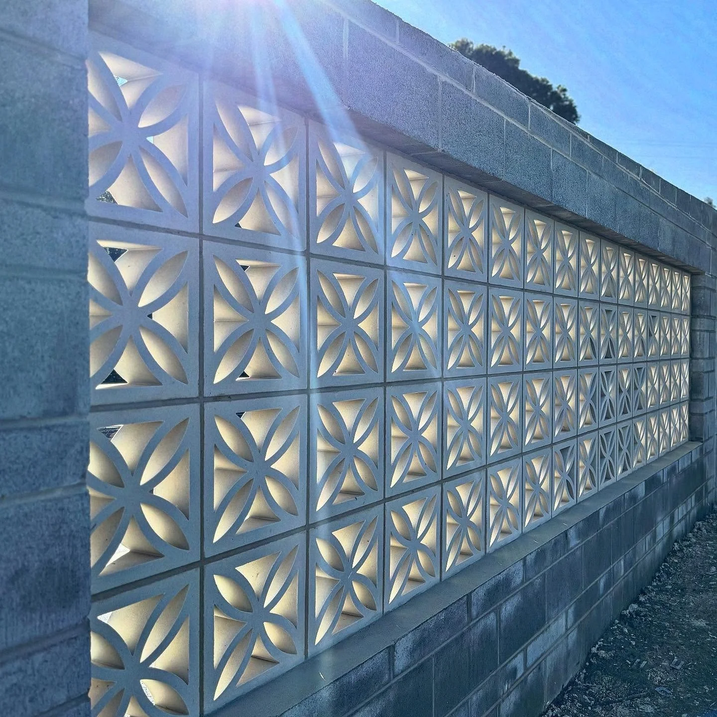 Decorative concrete block wall with geometric patterns and backlighting, sunlight shining from the top left