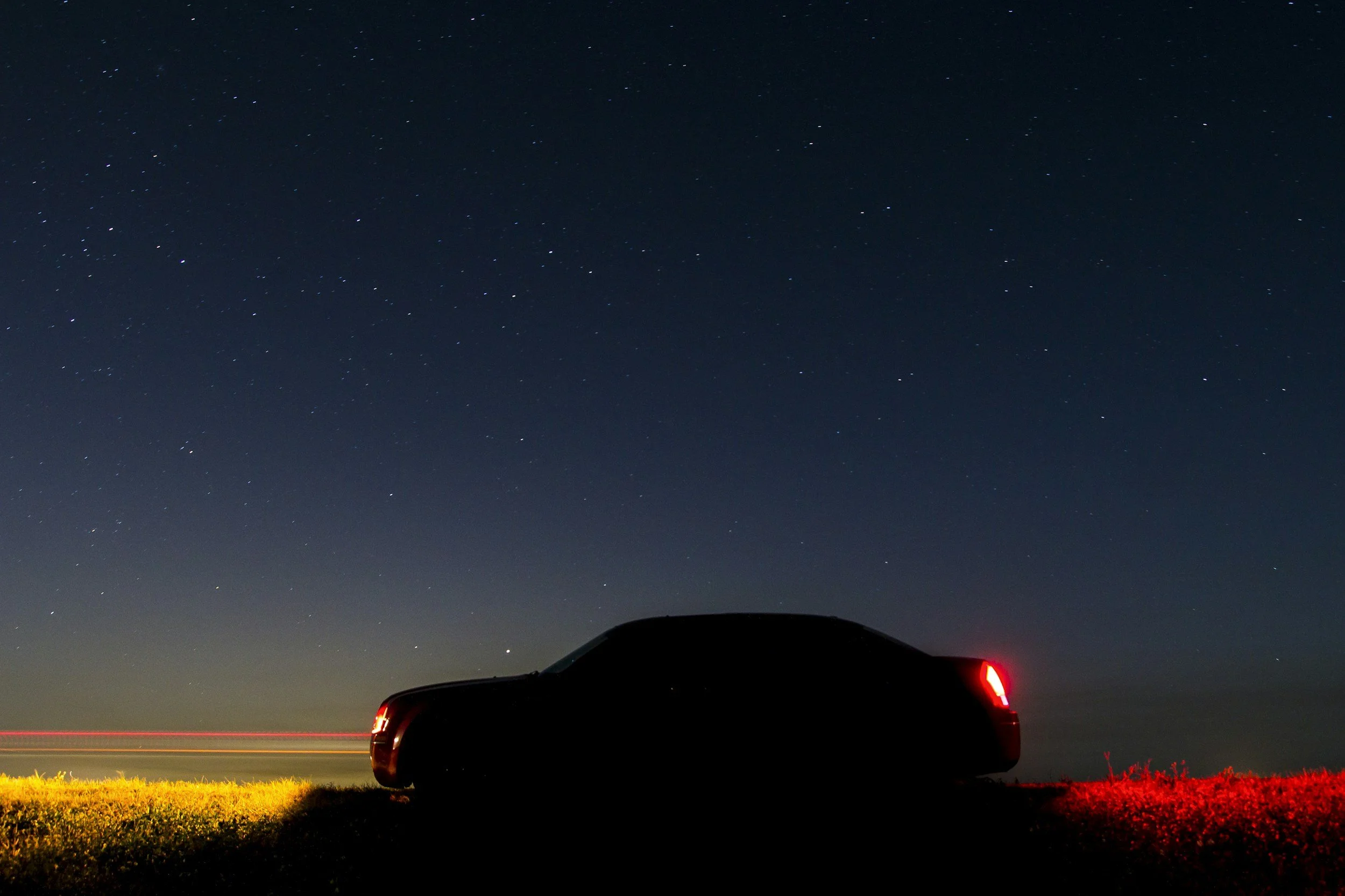 A black pickup truck parked on a grassy field under a starry night sky with distant hills visible.