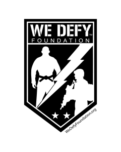 The We Defy Foundation logo featuring a shield with a silhouette of a person holding a weapon, a lightning bolt, and a smaller figure in a helmet, with the foundation's name and website.