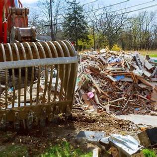 Pile of debris and wreckage outdoors with a large metal claw attachment nearby.