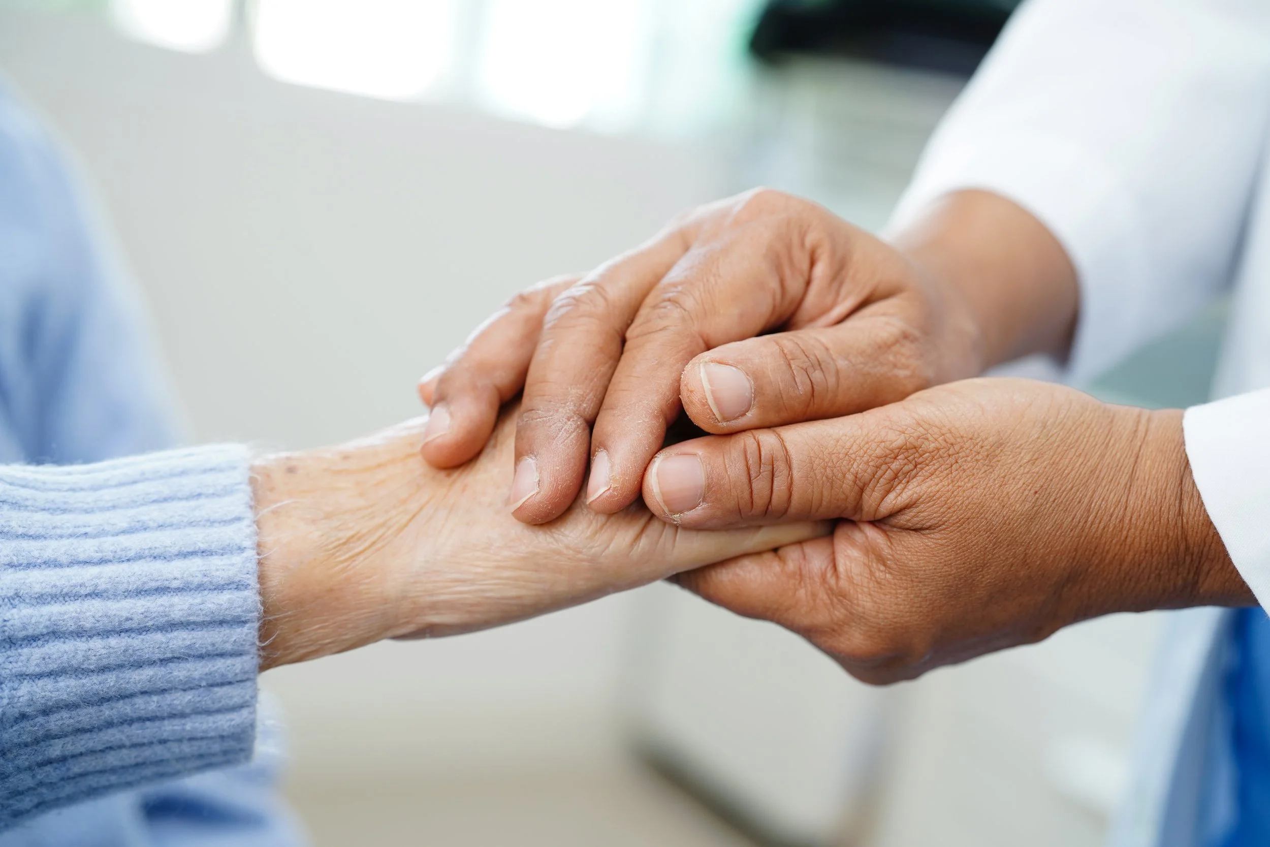 A person wearing a white coat holding the hand of an elderly person wearing a blue sweater.