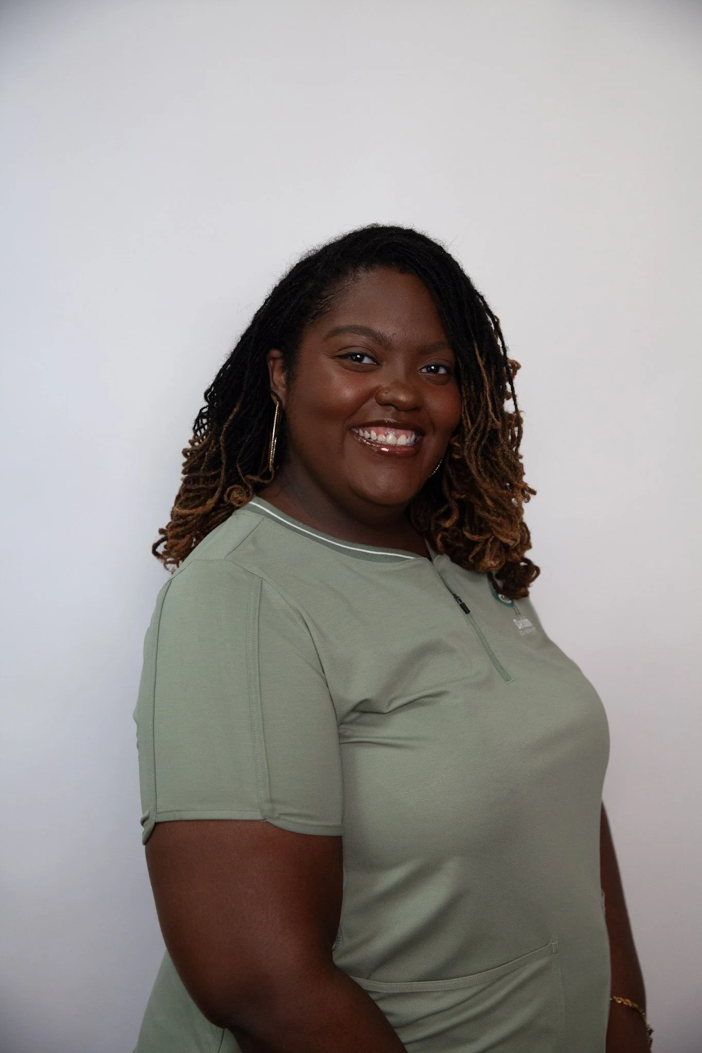 A smiling African American woman with shoulder-length curly hair, wearing a light green athletic shirt, standing against a plain white background.