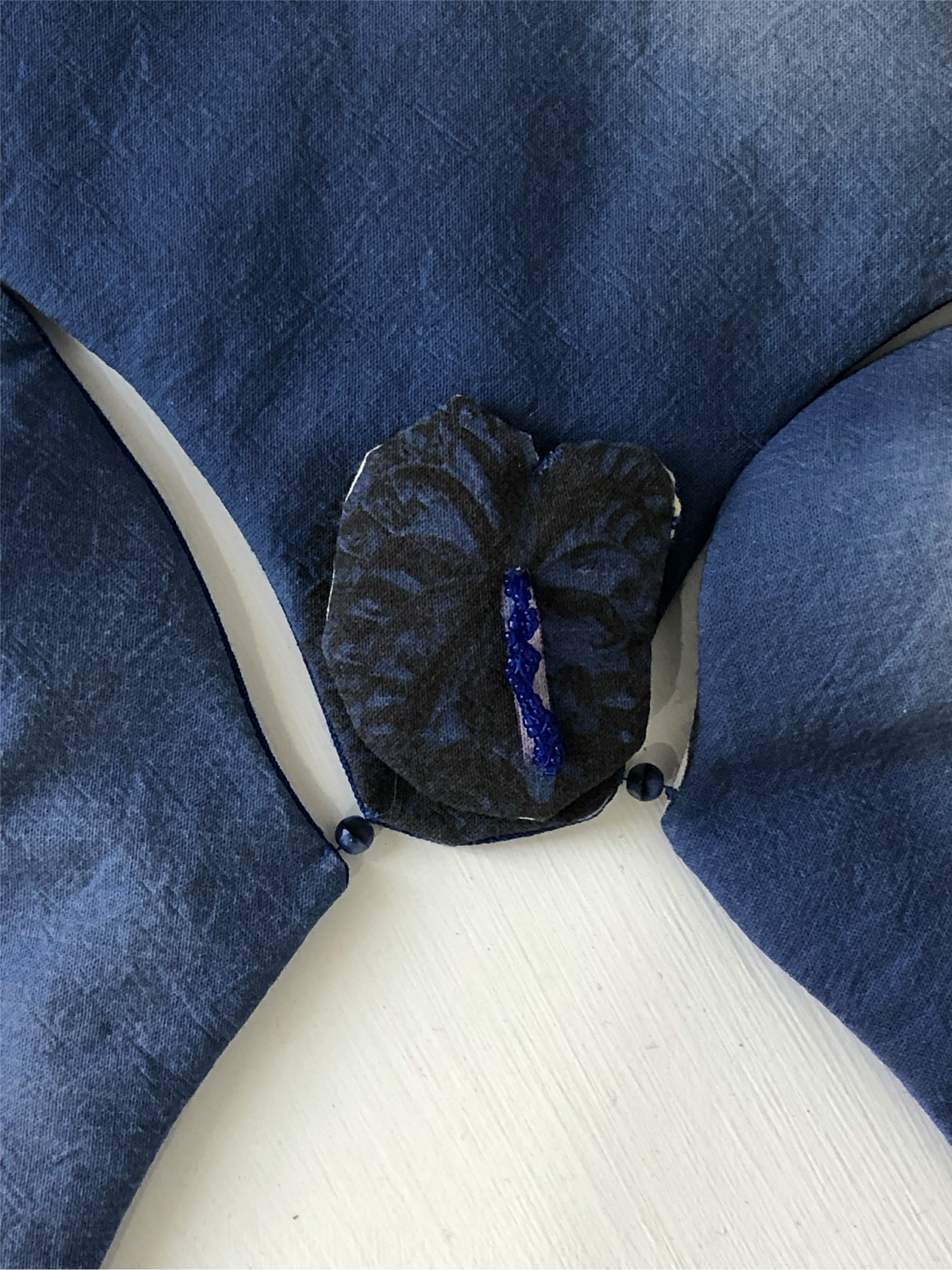 Close-up of a black and blue decorative object, possibly a piece of fabric or art, placed between the cushions of a blue upholstered chair with white trim.