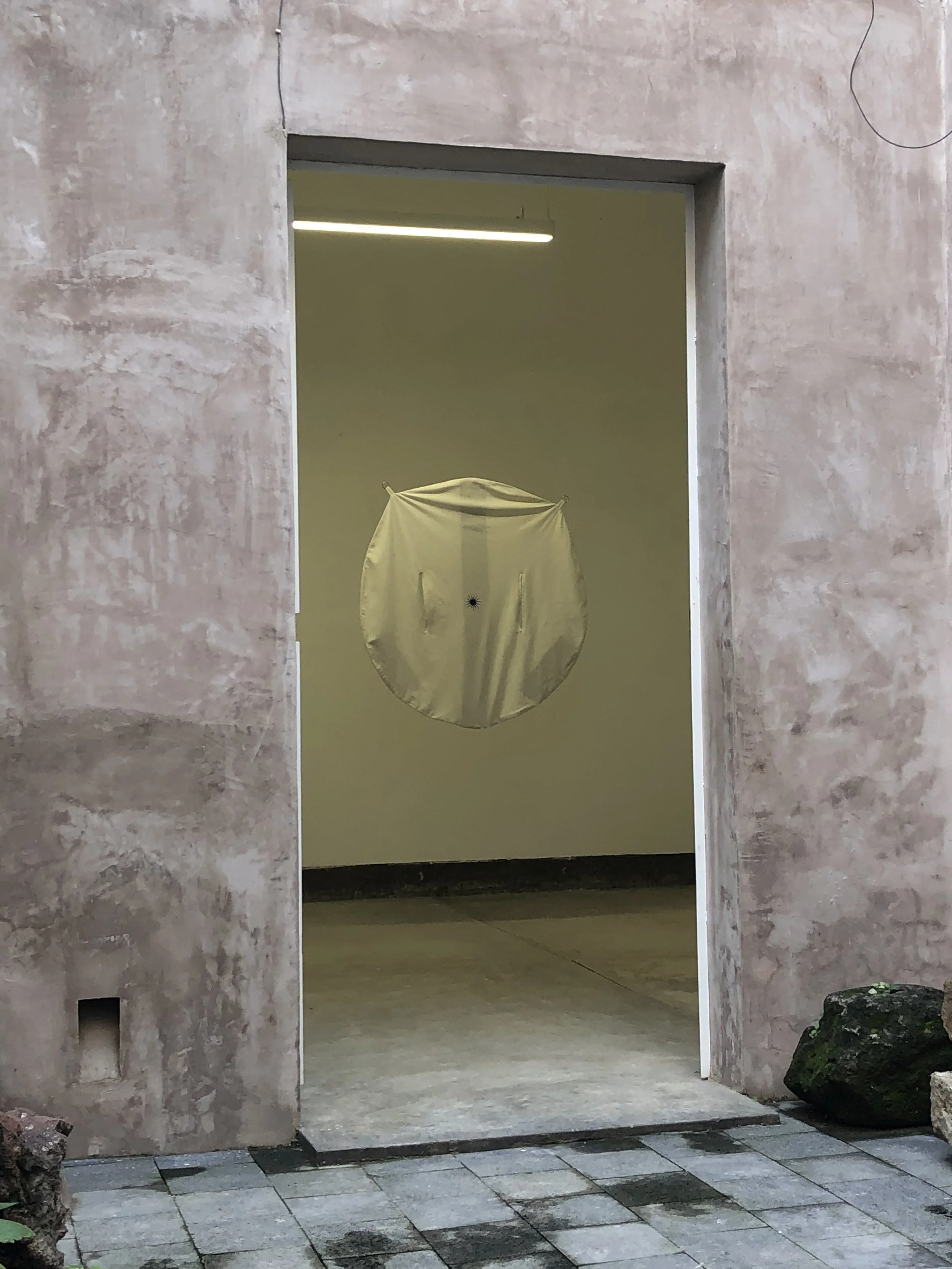An open doorway showing an art installation of a reflective circular sculpture hanging inside a gallery space.