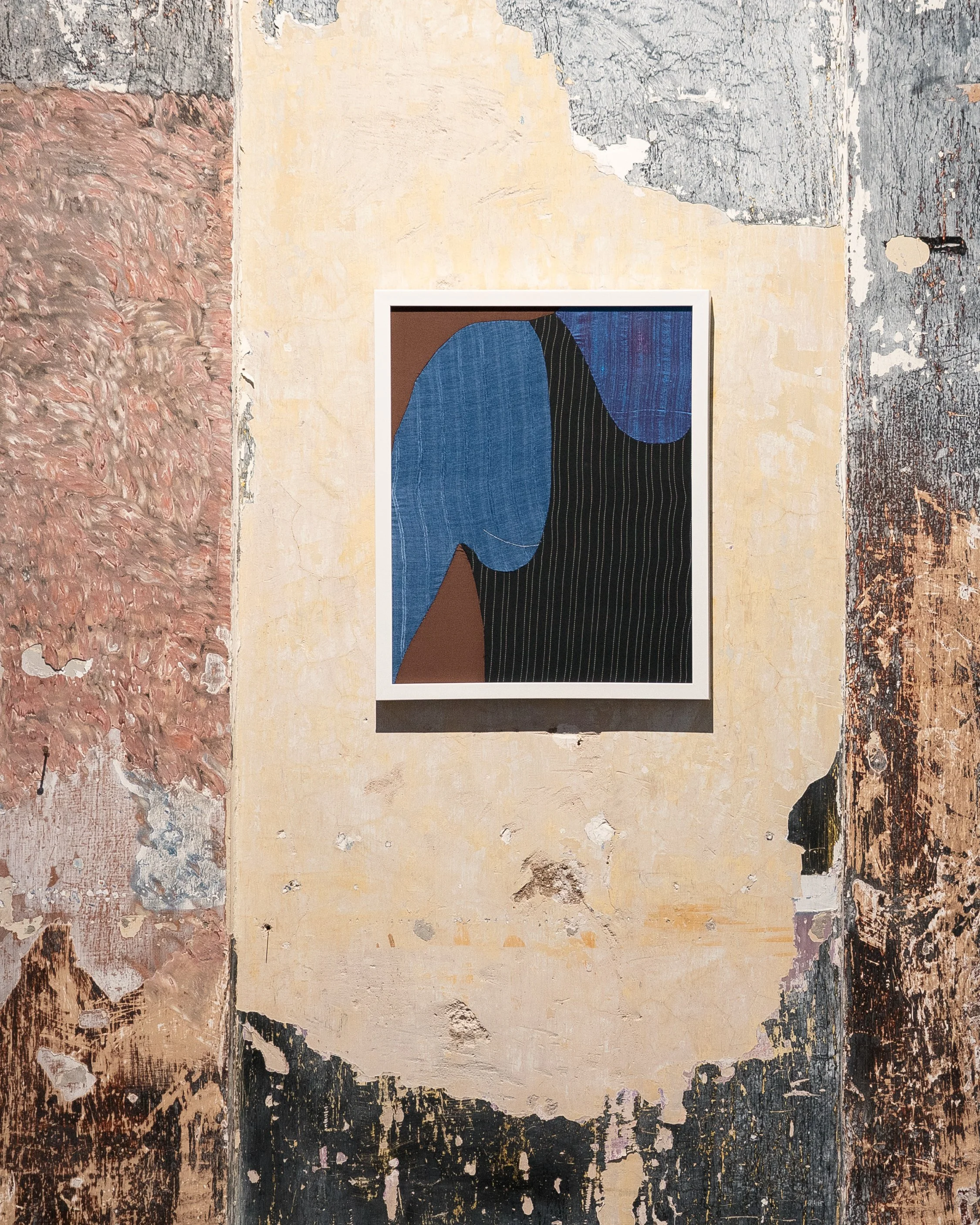 An abstract art piece with blue, black, brown, and dark green shapes on a textured background displayed on a distressed, weathered wall.