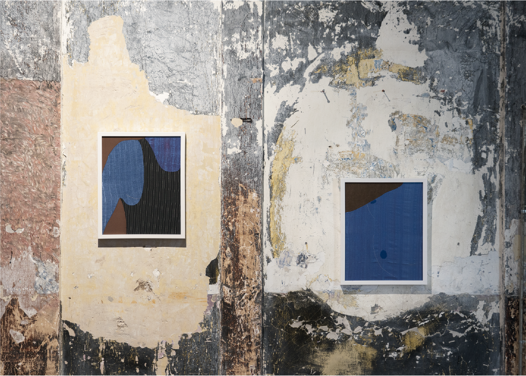 Two abstract art pieces on a weathered, textured wall with peeling paint and exposed plaster.