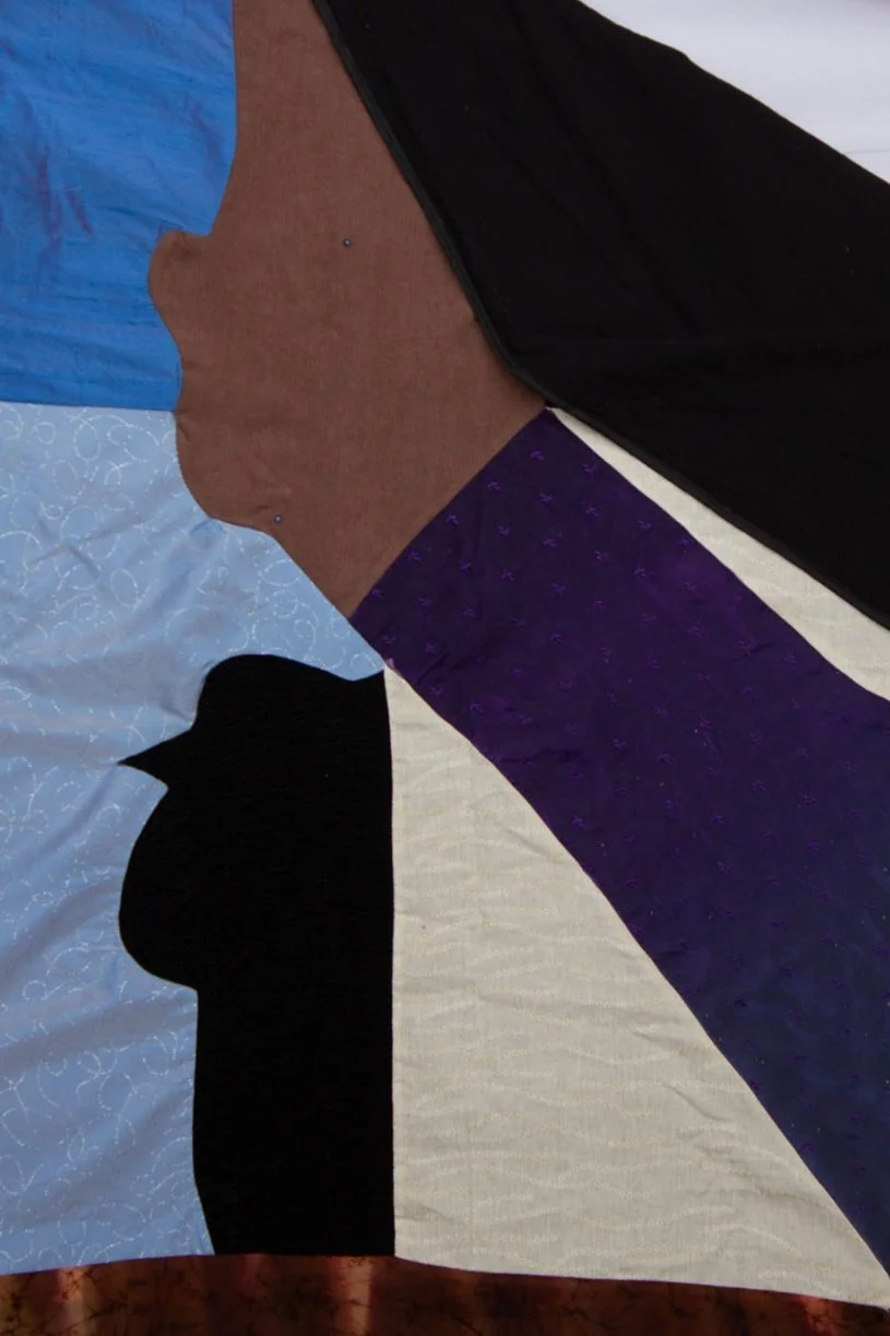 Close-up of a quilt with fabric pieces in various colors and patterns, including black, purple, blue, tan, and white.