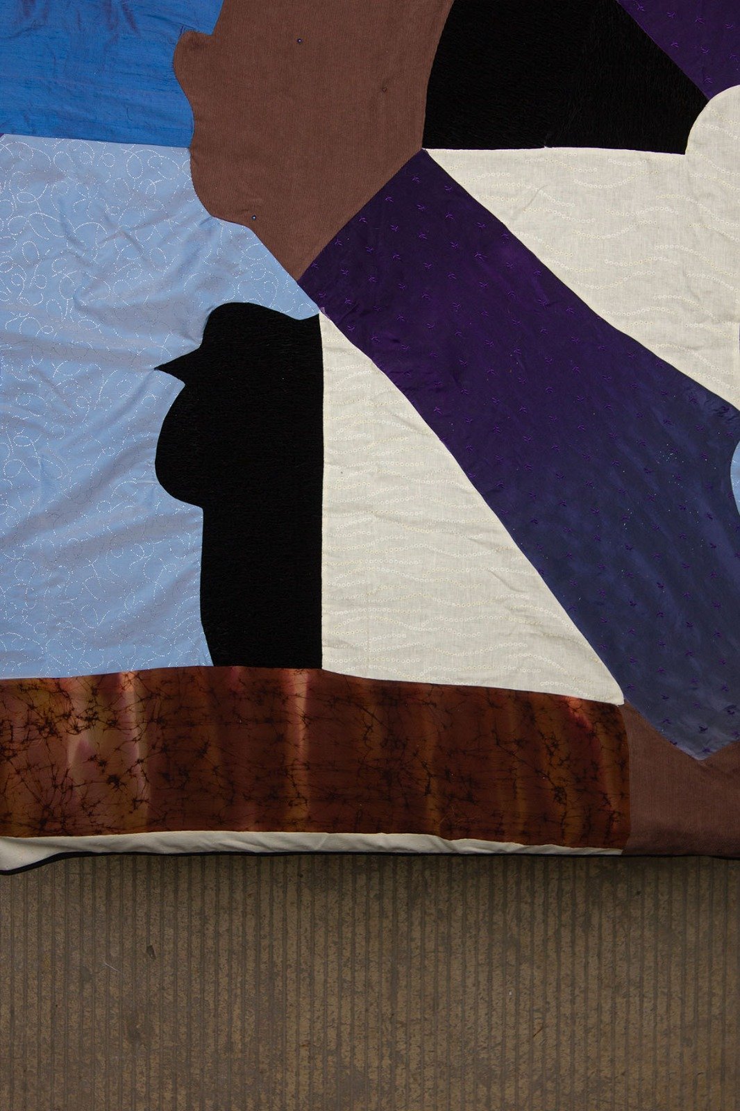 Close-up of a quilt with various fabric patches in different colors and patterns, arranged in an abstract, geometric design.