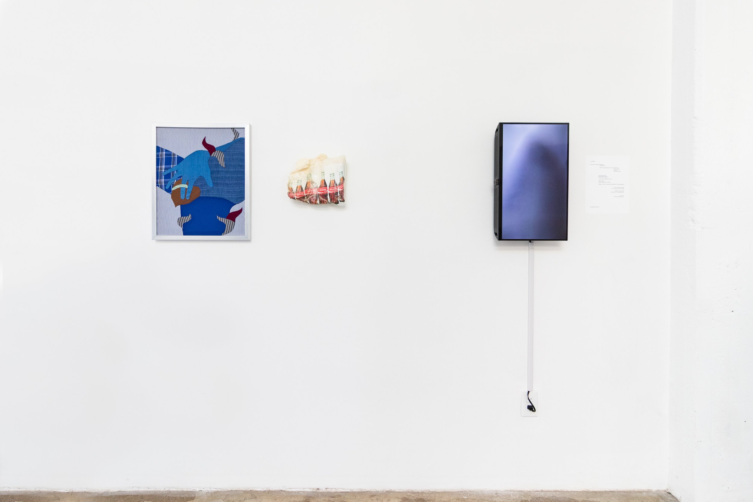 An art gallery wall features three artworks: a framed digital illustration of a figure with a blue face and plaid clothing, a textile piece with a row of red bottles, and a black flat-screen monitor on the wall, with a wire hanging down to an electrical outlet.