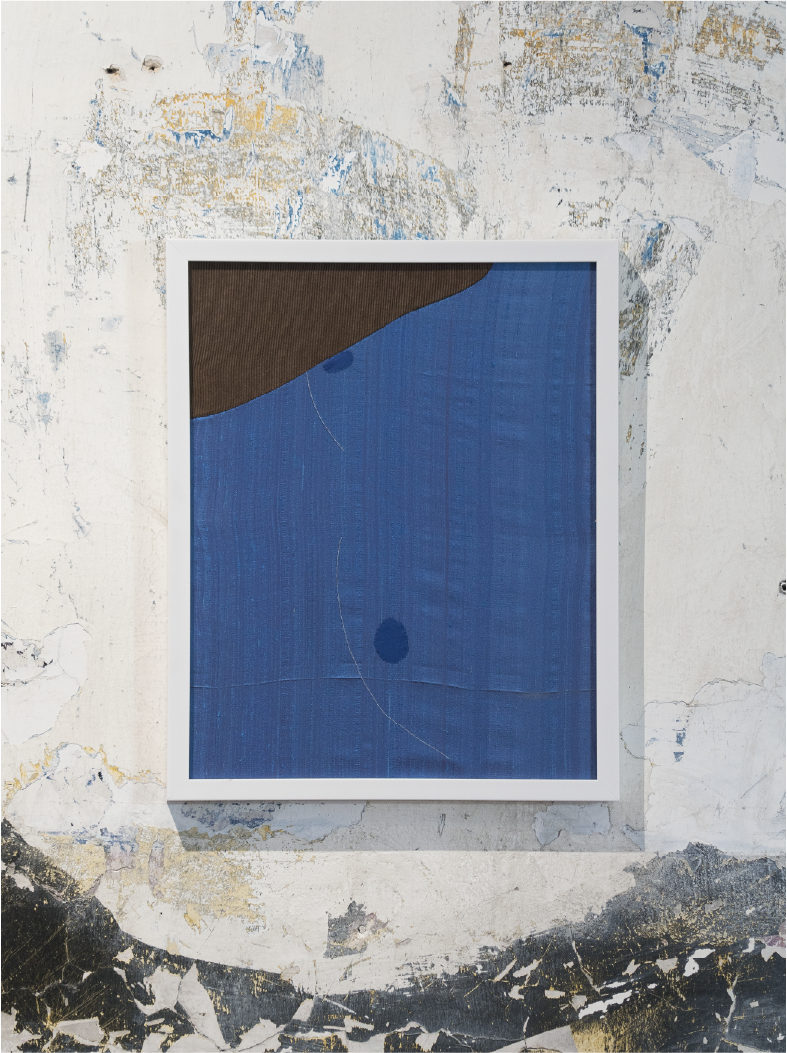 Abstract modern art piece with a large blue section, a smaller dark brown section in the top left corner, and a small dark blue circle, framed and hung on a worn, textured wall.