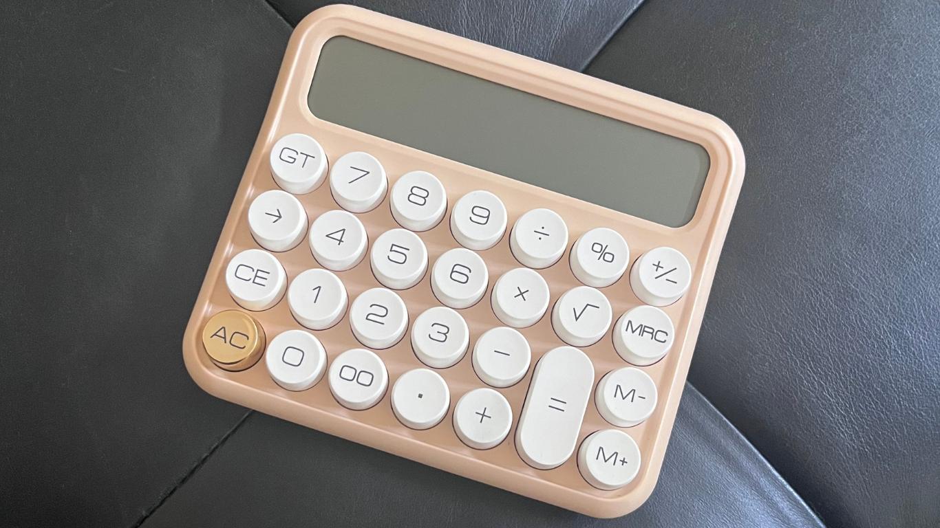 A pink calculator with white buttons and a gold "AC" button, resting on a black surface.