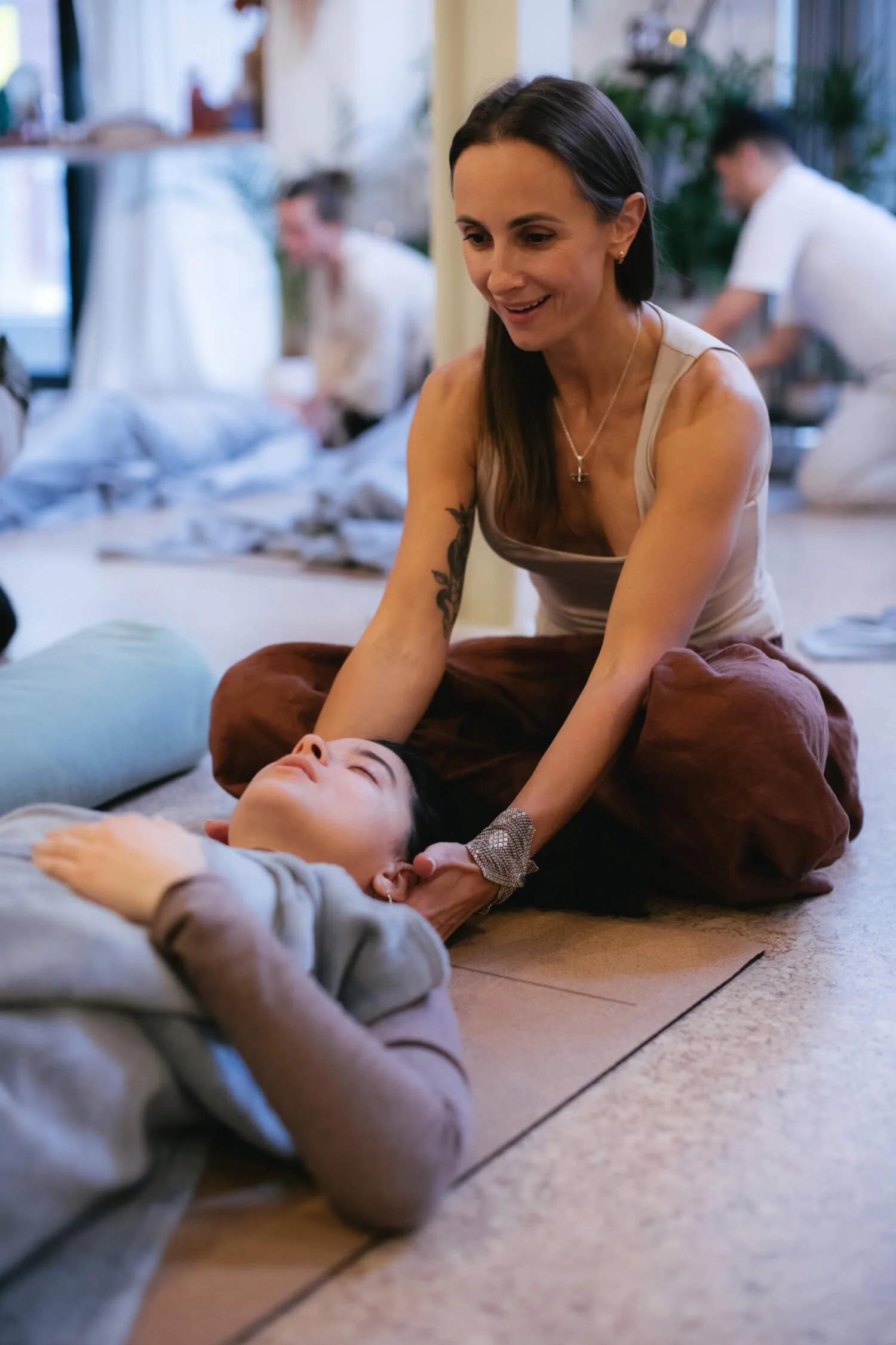 A woman receiving a Reiki session from a young girl on the floor in a cosy room with other people in the background.