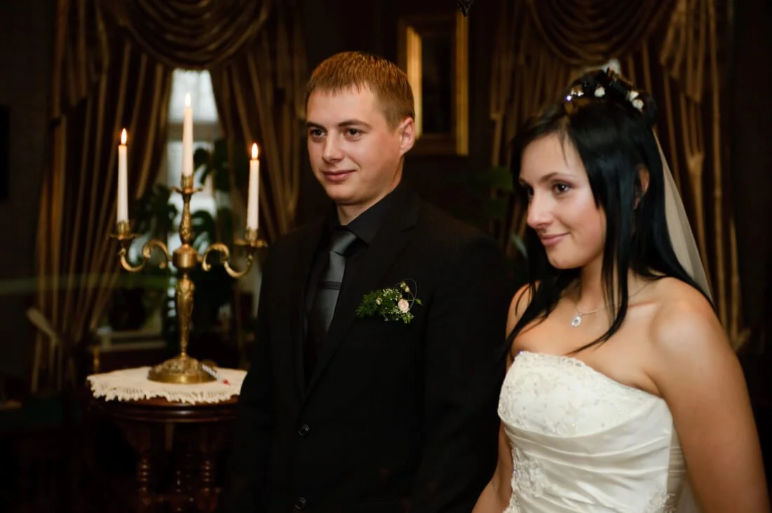 Bride and groom standing together at their wedding reception, with a candelabrum and curtains in the background.