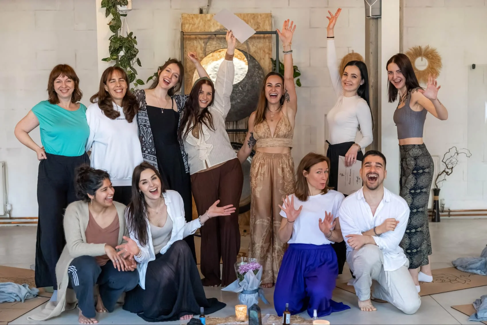 Group of people celebrating indoors, smiling, and posing for a photo, with some standing and some sitting on the floor.