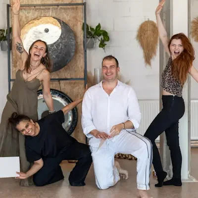 Five people posing and smiling in a bright, modern room with decorative plants and a yin-yang artwork on the wall. Holding certificates showing that they became Kundalini Activation Facilitators trained by Natalia Bareikis.