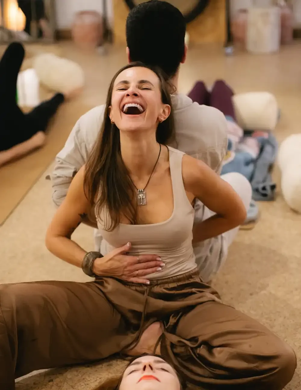 smiling woman is sitting on a cork floor with a gentleman behind her and they are holding hands, another person is laying peacefully by her side.