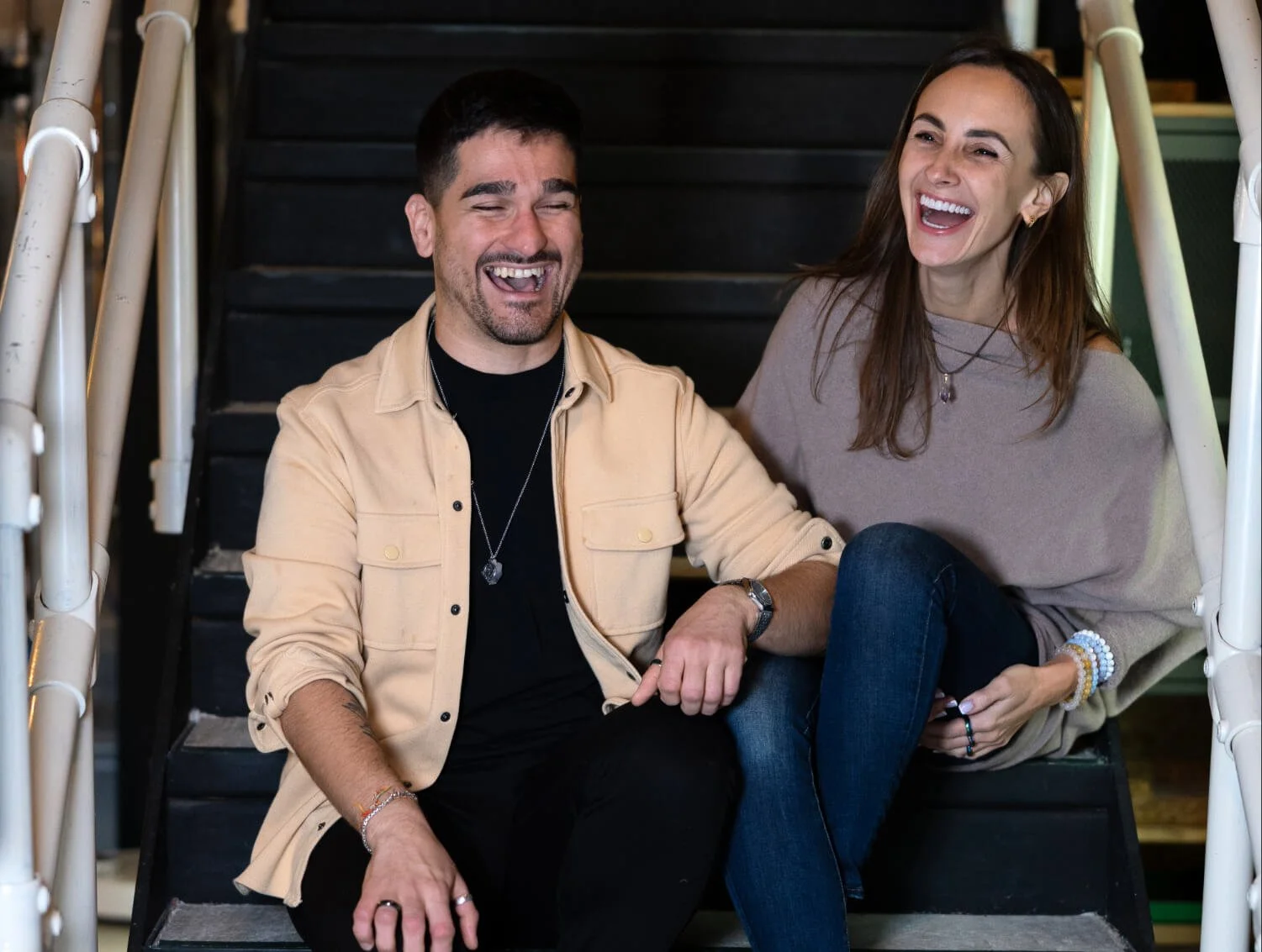 A man and a woman sitting on stairs, smiling and laughing together, holding hands.