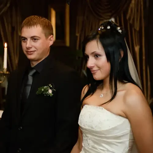 Bride and groom standing together at their wedding reception, with a candelabrum and curtains in the background.