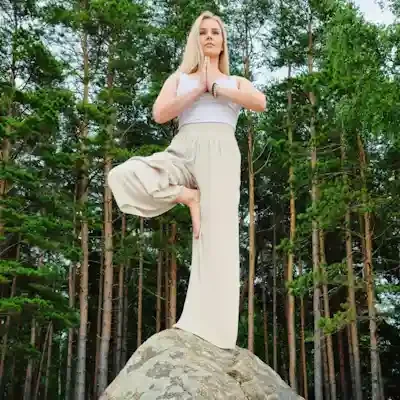 A woman practicing yoga in a tree pose on a large rock in a forested area.