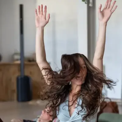 A woman in a lotus pose with her arms raised above her head in a blissful state in a calm studio with cork flooring.