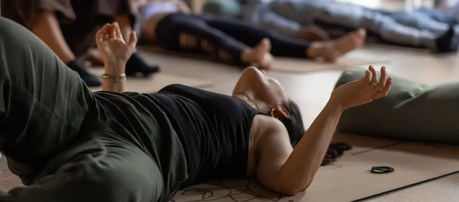 People lying on the floor during a yoga or meditation class, with some participants in a reclined position and others in a seated or extended pose.