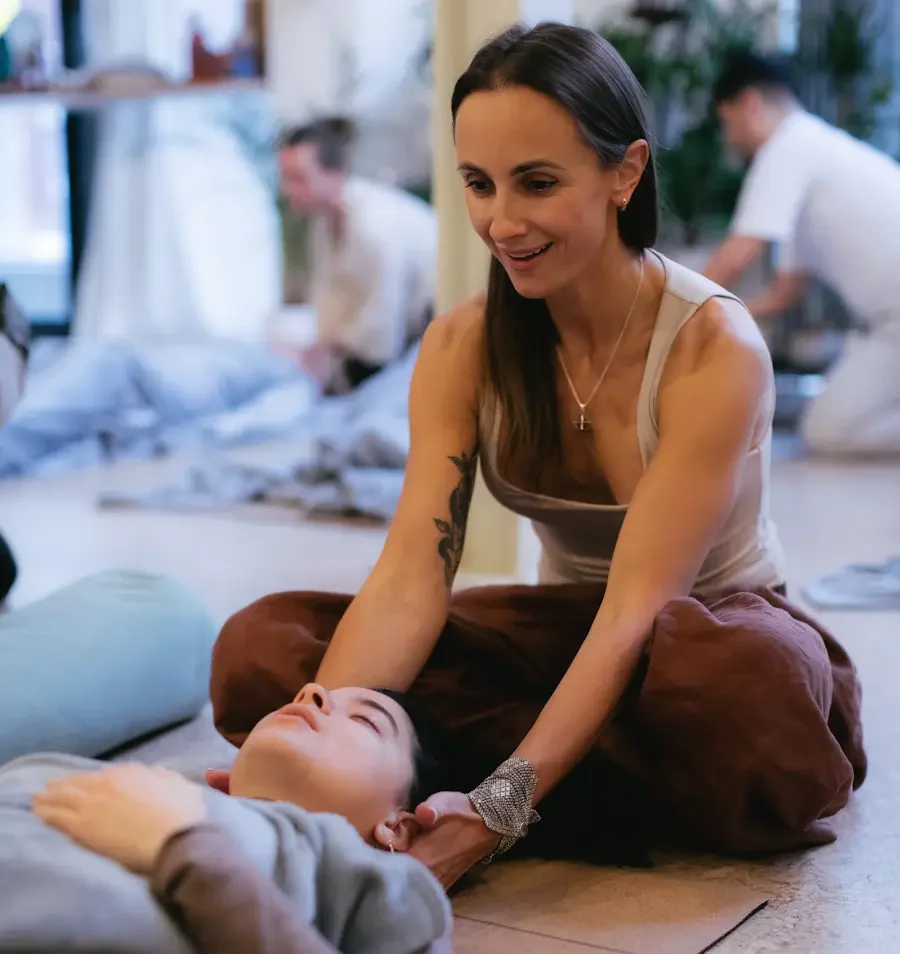 A woman receiving a Reiki session from a young girl on the floor in a cosy room with other people in the background.