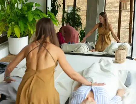 Woman is holding her hands on heart area on other two women which are laying on the floor, more people are on background.