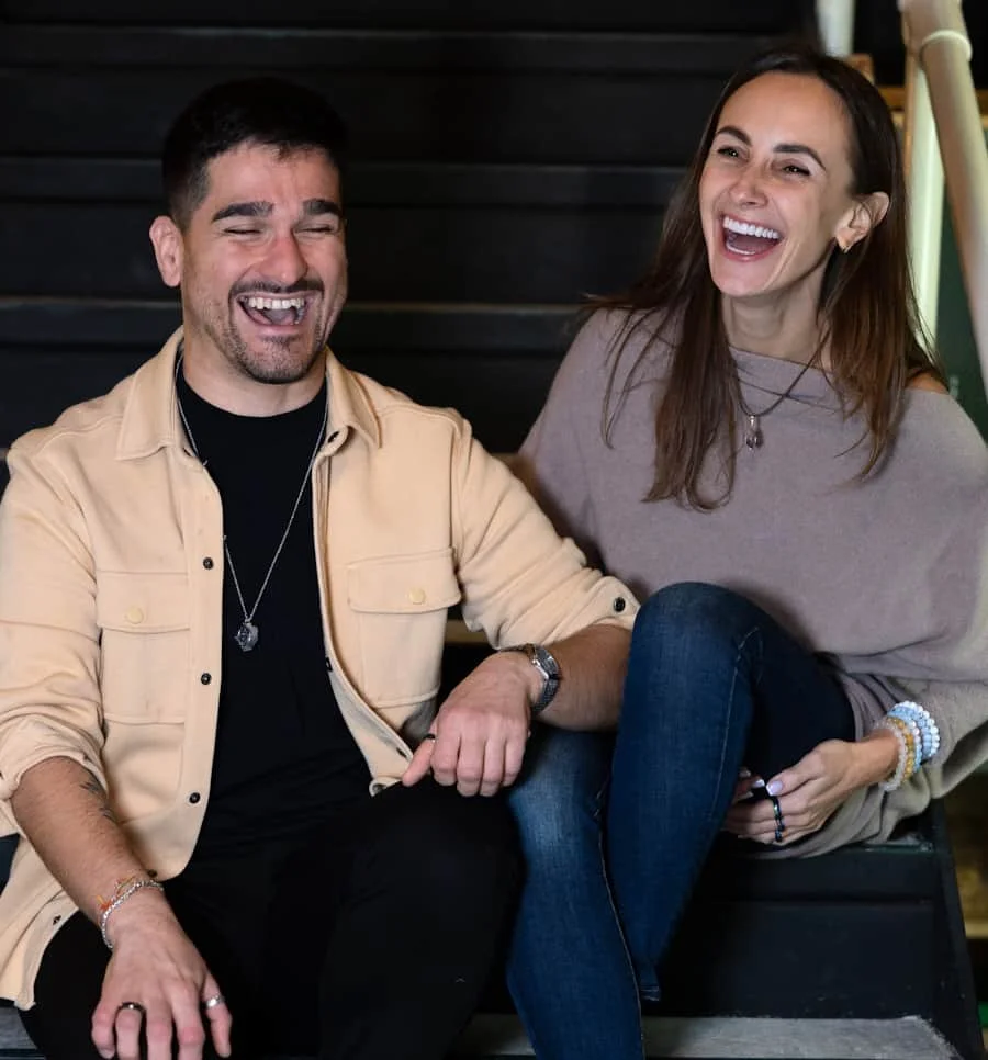 A man and a woman sitting on stairs, smiling and laughing together, holding hands.