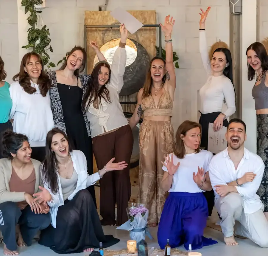 Group of people celebrating indoors, smiling, and posing for a photo, with some standing and some sitting on the floor.