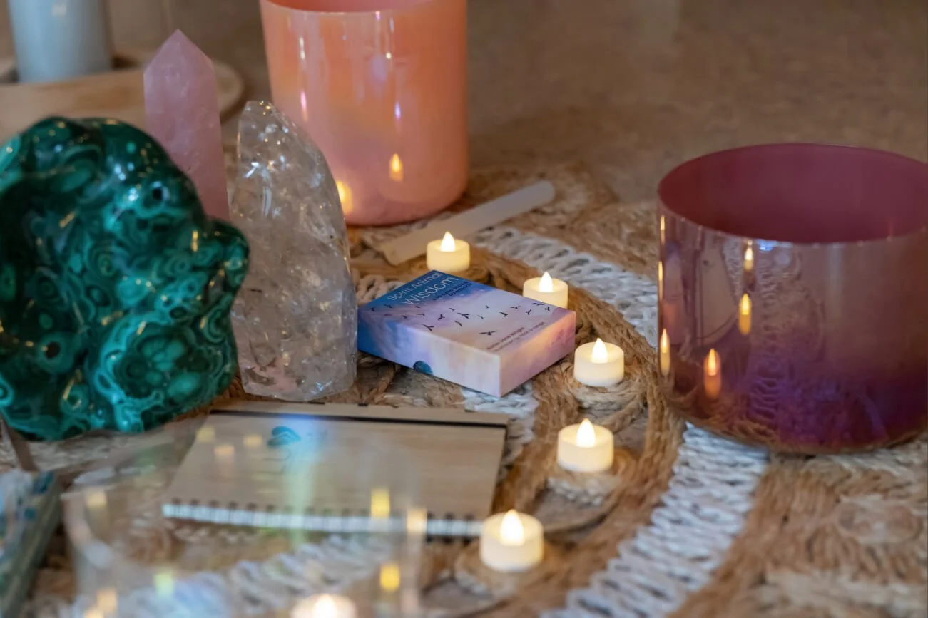 Decorative setup with crystals, candles, and a box on a woven surface. Notepad which says LUV YOURSELF by Natalia.