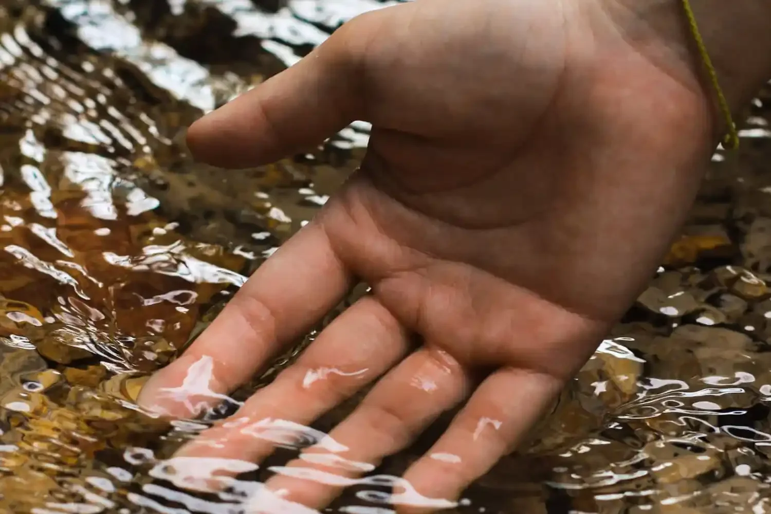 Hand in gently running water with very clear stones underneath
