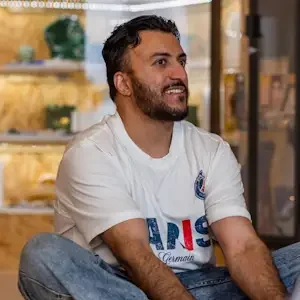 A man sitting on the floor with a smile on his face in a serene studio with crystals behind him.