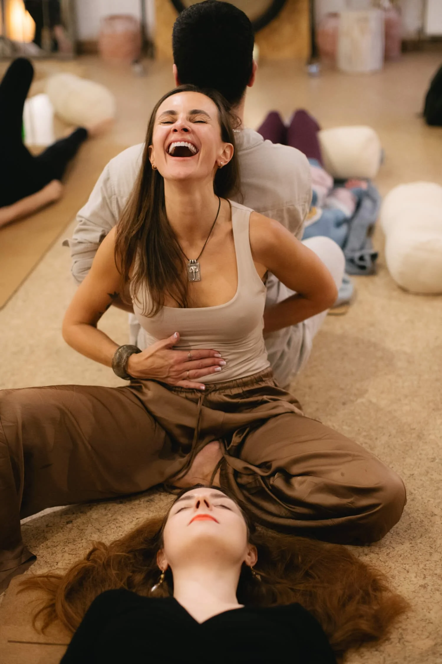 smiling woman is sitting on a cork floor with a gentleman behind her and they are holding hands, another person is laying peacefully by her side.