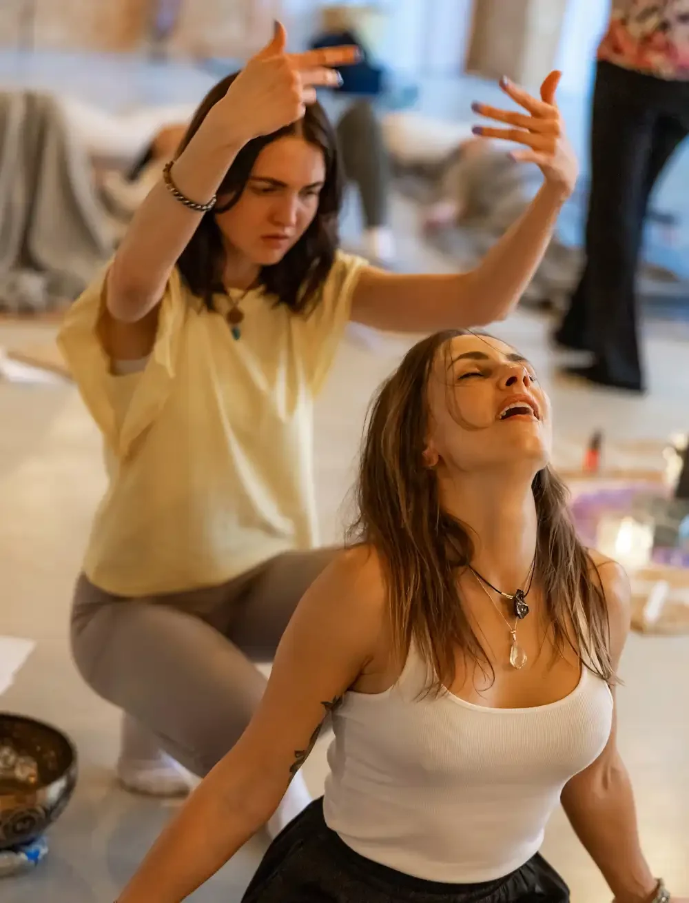 Two women in activation with peaceful faces and energy being present in a room, other people are behind them in activation process